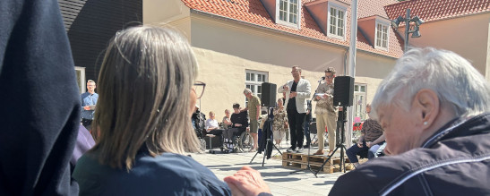 En kvinde holder tale og tegnsprogstolkes. Kameravinkelen er over skuldrene på to, der bruger taktilt tegnsprog